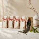 A row of small tea favour pouches tied with coral ribbon, one open with green tea leaves spilling out